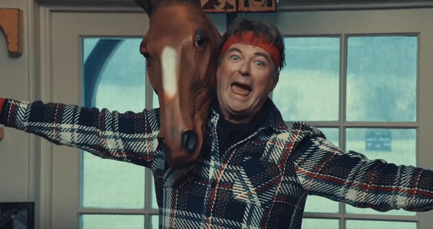 screenshot of Julian Clary on Taskmaster with a rubber horse head on his shoulder and a silly expression.